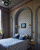 A stately bedroom designed by MBDS featuring Fresco in Dark Indigo used as both wall panelling and a bedspread. The diamond-square pattern creates a dramatic, layered effect behind the bed, adding depth and artistry to the space. A canopy in Boundary Ochre crowns the bed, blending modern grandeur with graphic elegance.
